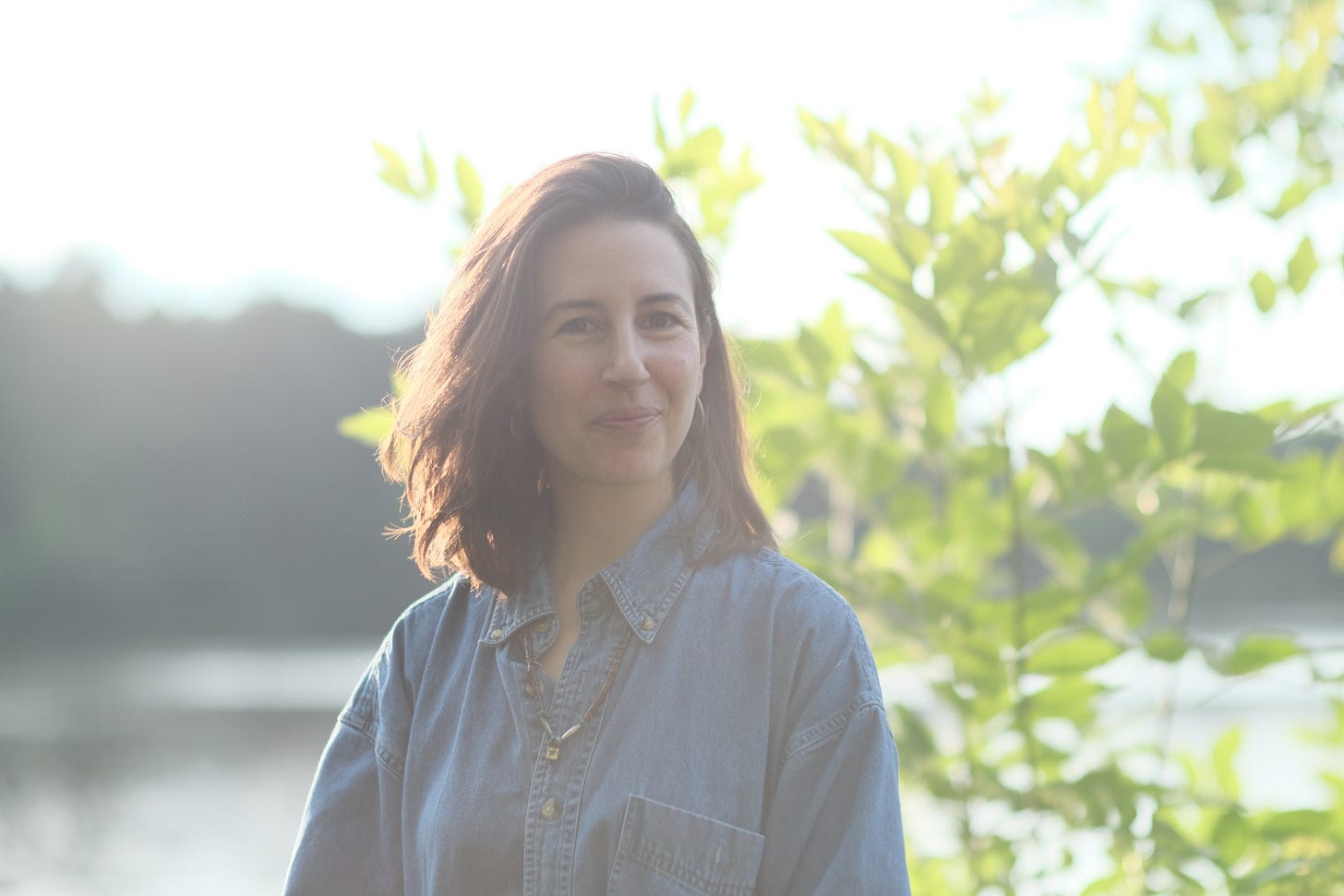 A white woman with brown hair stands in front of a lake.