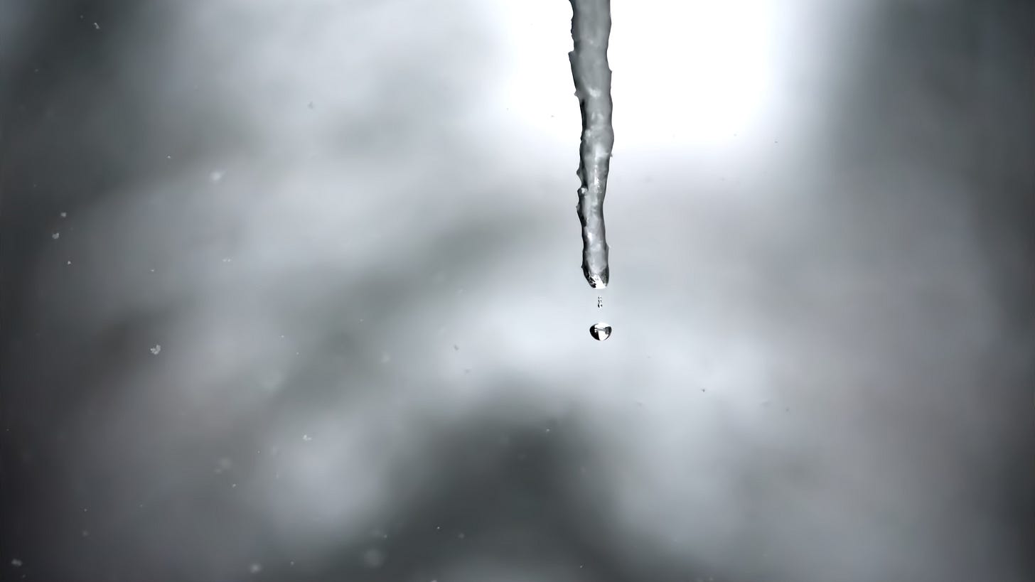 As snow flurries, a droplet begins its journey from the bottom of a melting icicle.