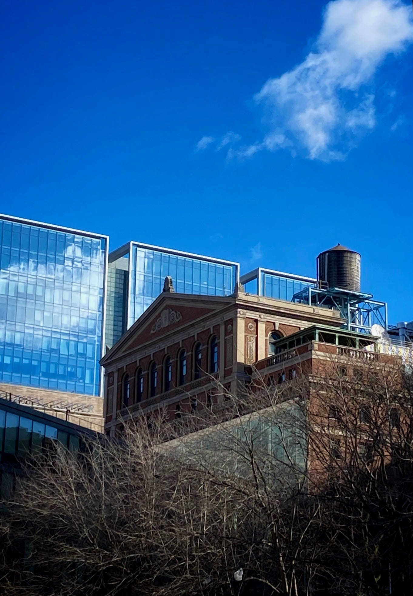 A water tower sits on a stately brick building. Behind it a modern glass building reflecting the deep blue sky and the few clouds.