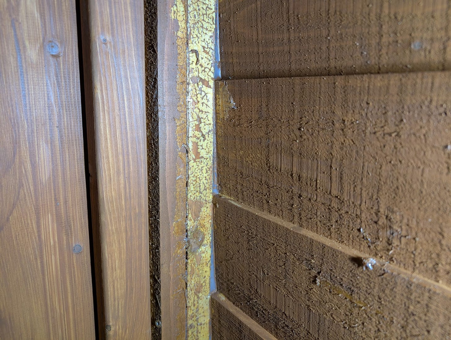 Close-up photo of a painted shed wall, showing a visible white sealant line that did not take the paint colour.