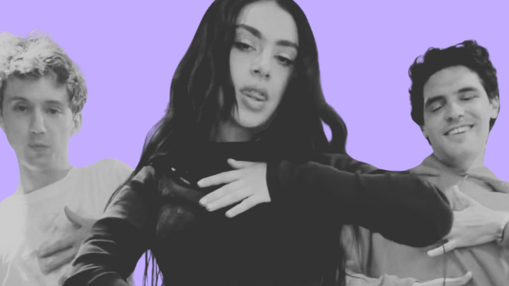 Monochrome image with a purple background featuring three people. In the center is Charli XCX, a woman with long, dark hair wearing a dark top. She has her hand raised near her chest in a dancing pose, with a relaxed expression on her face. To her left is Troye Sivan, a man with short, curly hair, wearing a light shirt and also posing with his hand raised. To her right is another man with short, dark hair, smiling with his hand raised in a similar pose.