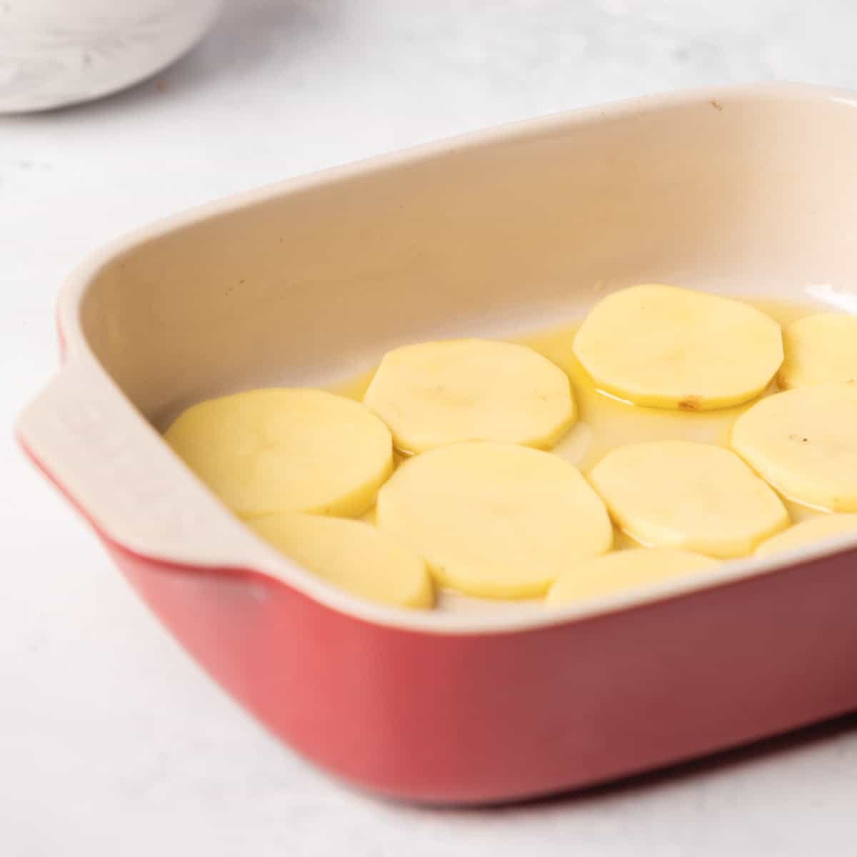 Sliced potatoes layer on bottom of baking dish.