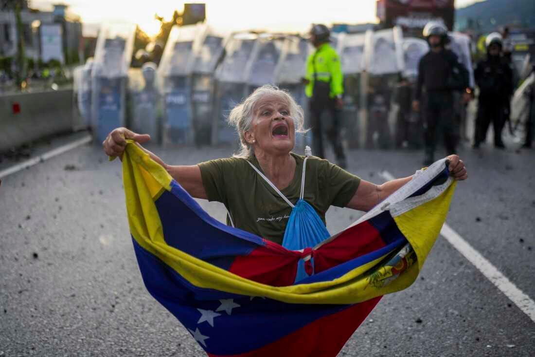 Consuelo Marquez holds a Venezuelan flag in front of police blocking demonstrations against the official election results declaring President Nicolás Maduro's reelection, the day after the vote in Caracas, Venezuela, Monday.