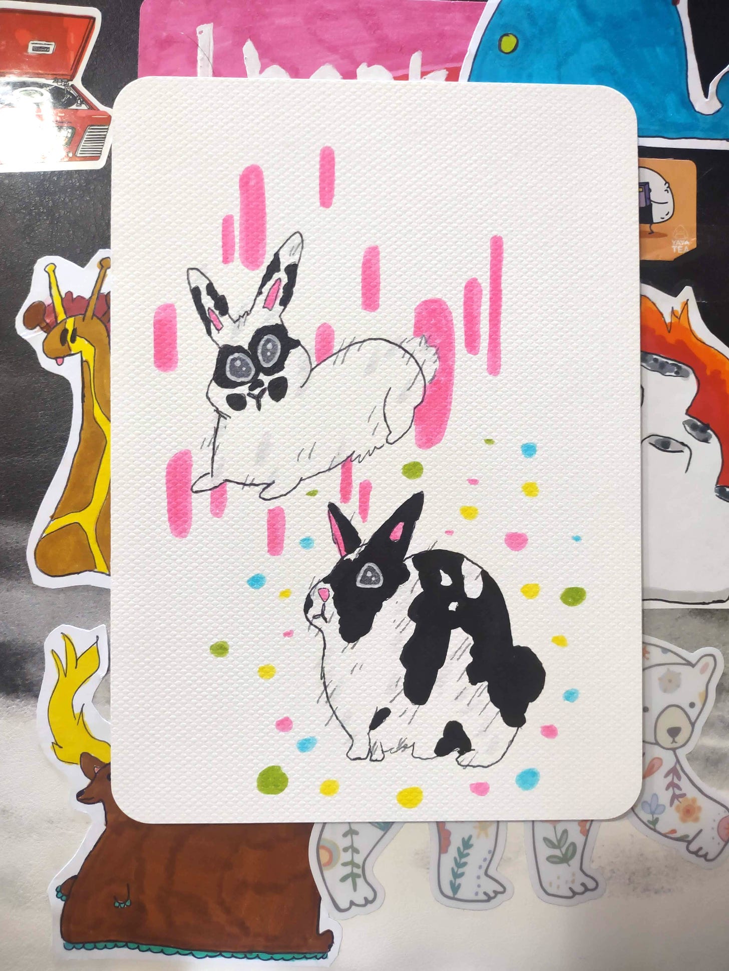 A cartoony illustration of two black and white bunnies with stickers of other illustrated animals in the background.