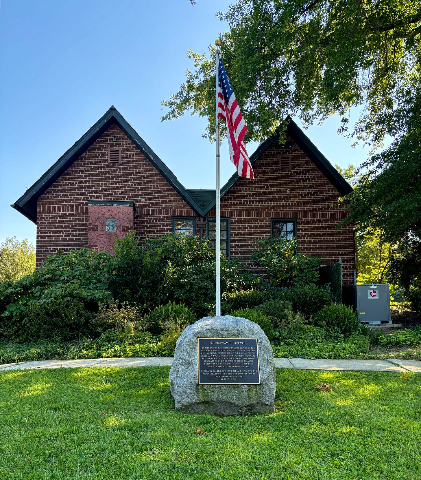 An American flag in a rock with a plaque on its front in front of a brick building.