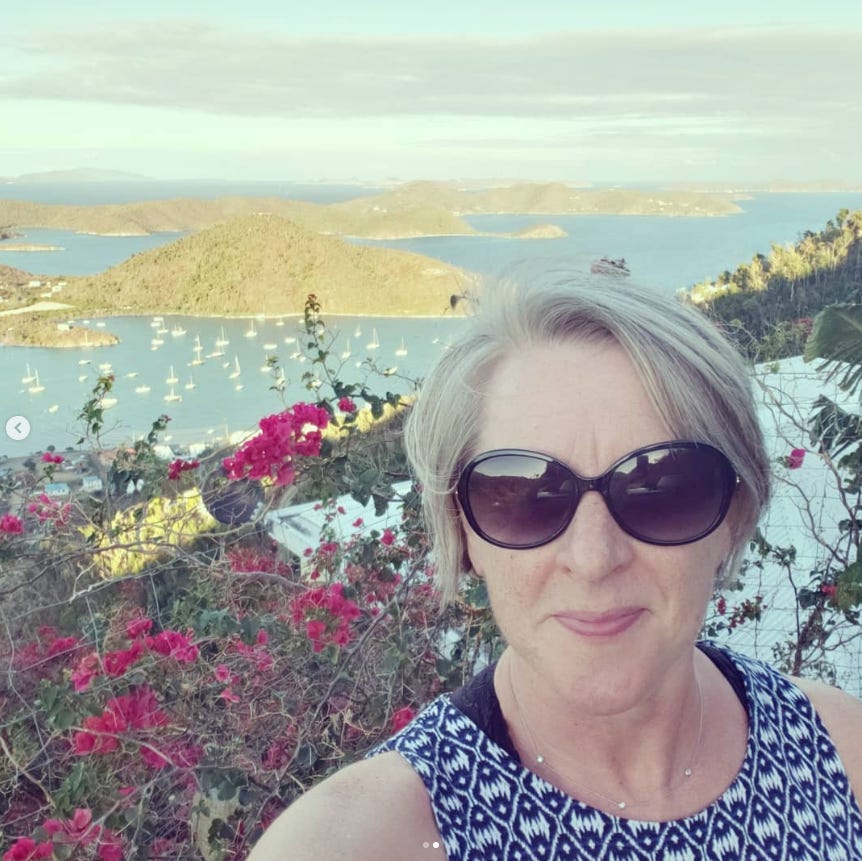 Woman with short hair and sunglasses in a selfie with red flowers and carribean islands in the background