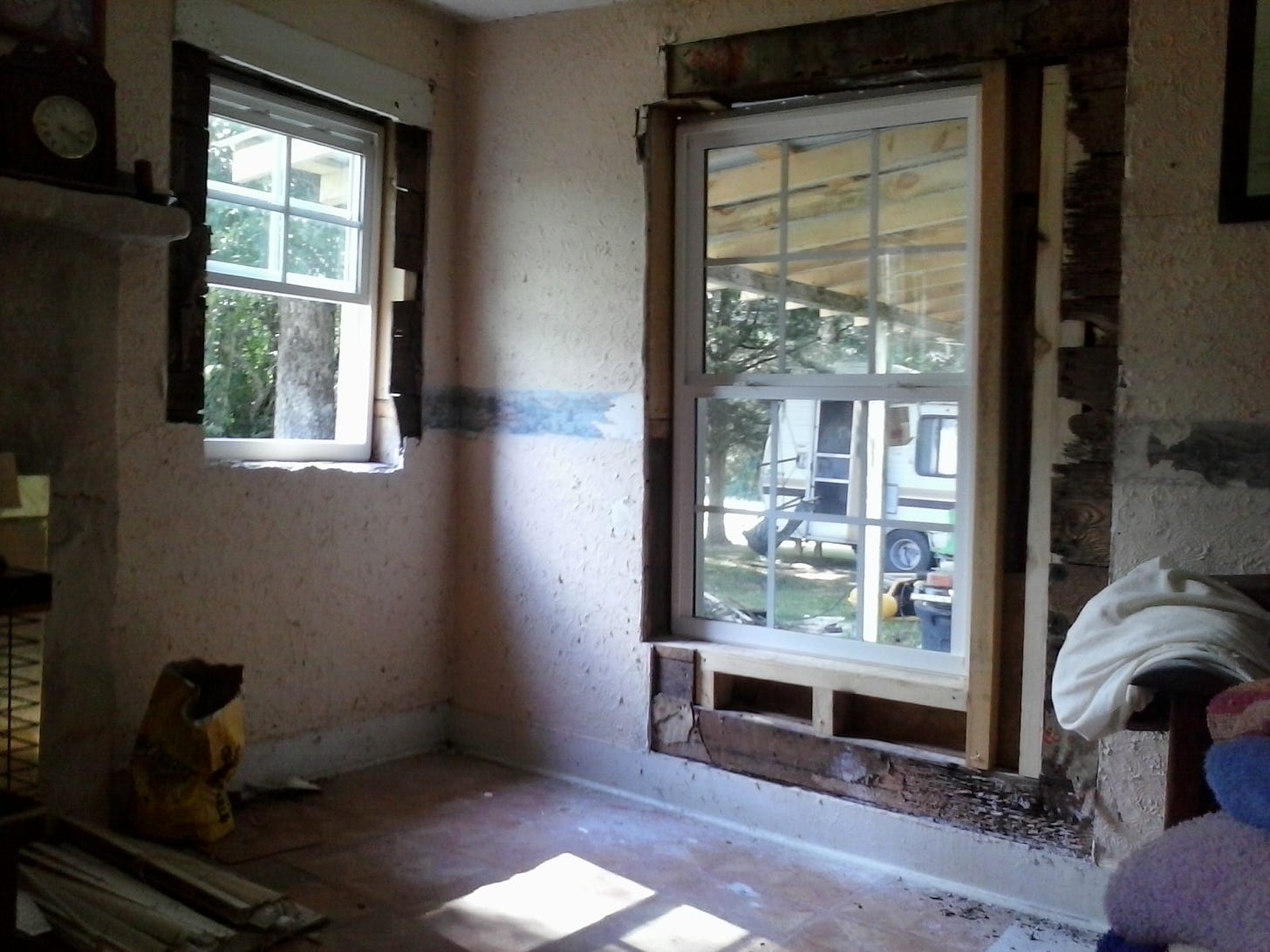 A corner of a room, with a small window on one wall and a larger window on the other wall. The windows are unframed, and the room is obviously under construction