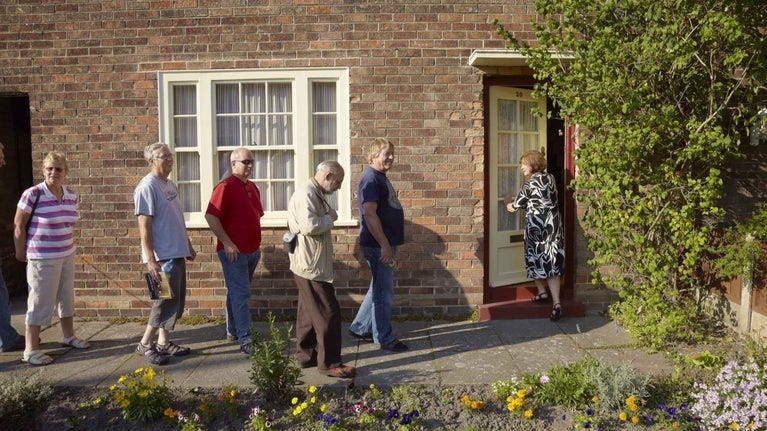 Five visitors outside the brick front of Paul McCartney's childhood home, of 20 Forthlin Road, Liverpool.