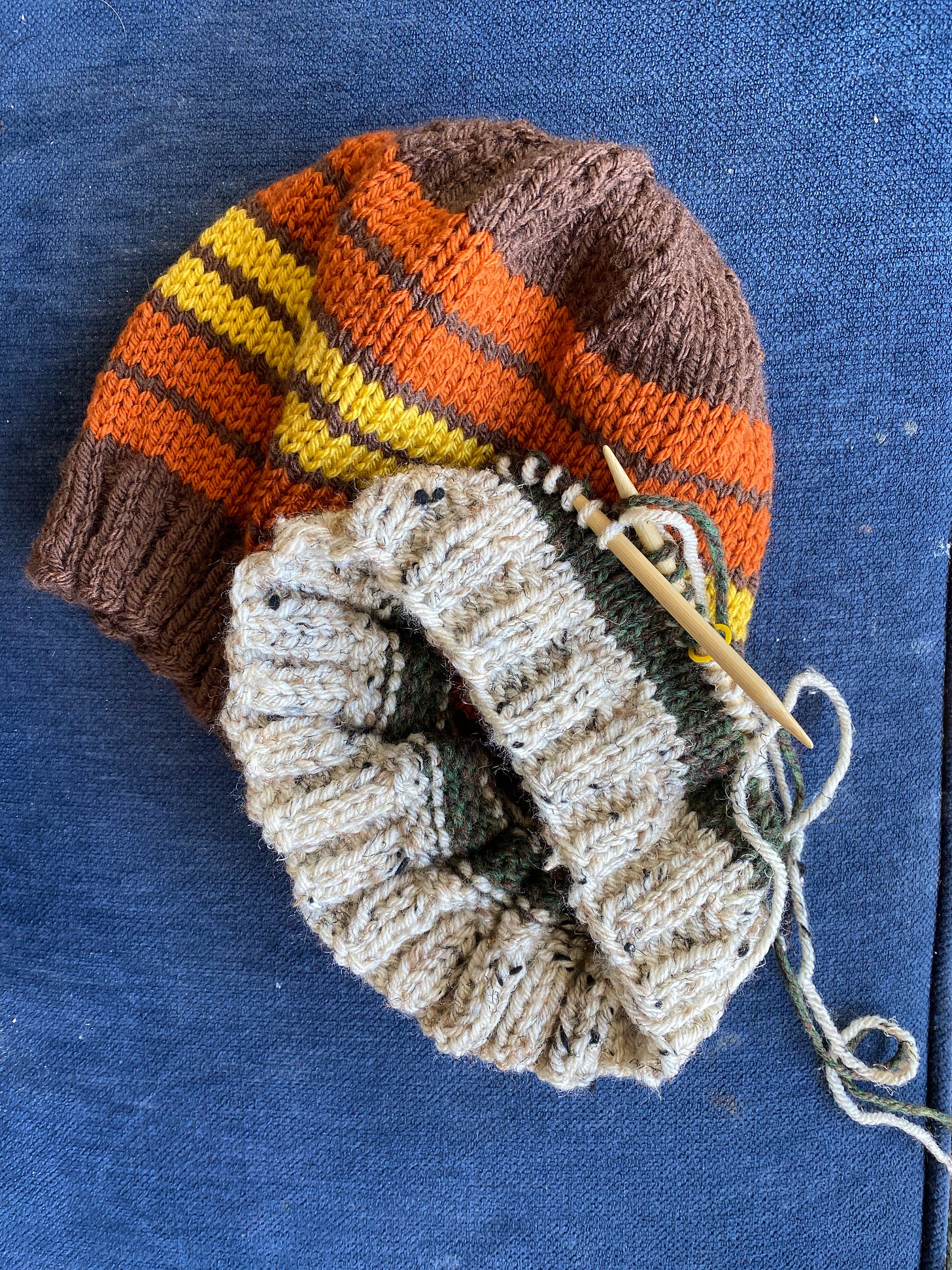 Handknit beanies. A completed on in shades of orange and one just started in oatmeal tweed and dark green.