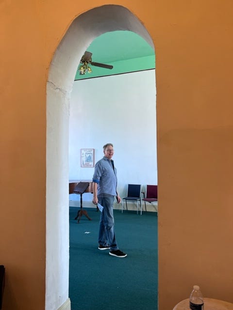 Orange wall with an irregular, narrow arch cut into it and my husband behind the arch