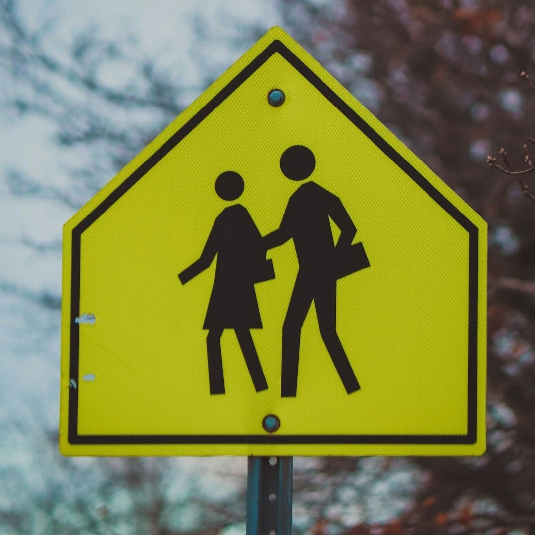 a yellow pedestrian crossing sign with a tree in the background a yellow pedestrian crossing sign with a tree in the background