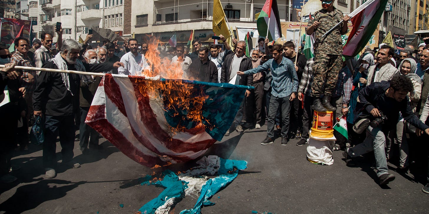 Demonstrators burn a US and an Israeli flag during the funeral for seven Islamic Revolutionary Guard Corps members killed in a strike in Syria, which Iran blamed on Israel, in Tehran on April 5, 2024. The Guards, including two generals, were killed in the air strike on April 1, which levelled the Iranian embassy's consular annex in Damascus. The funeral ceremony coincides with the annual Quds (Jerusalem) Day commemorations, when Iran and its allies stage marches in support of the Palestinians. (Photo by Hossein Beris / Middle East Images / Middle East Images via AFP) (Photo by HOSSEIN BERIS/Middle East Images/AFP via Getty Images)