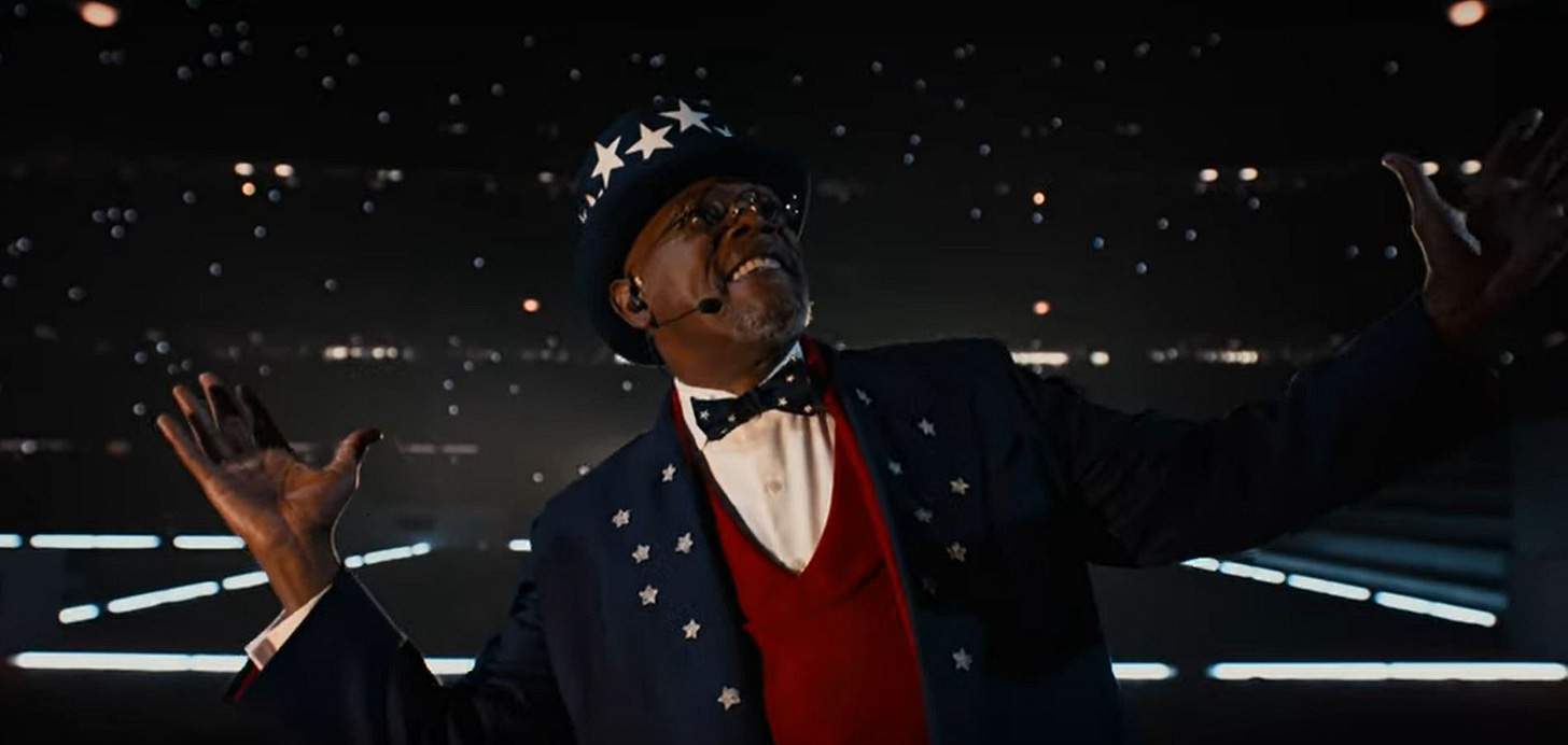 An elder Black man wearing glasses, a dark blue top hat with white stars and matching suit welcomes a crowd off-screen.