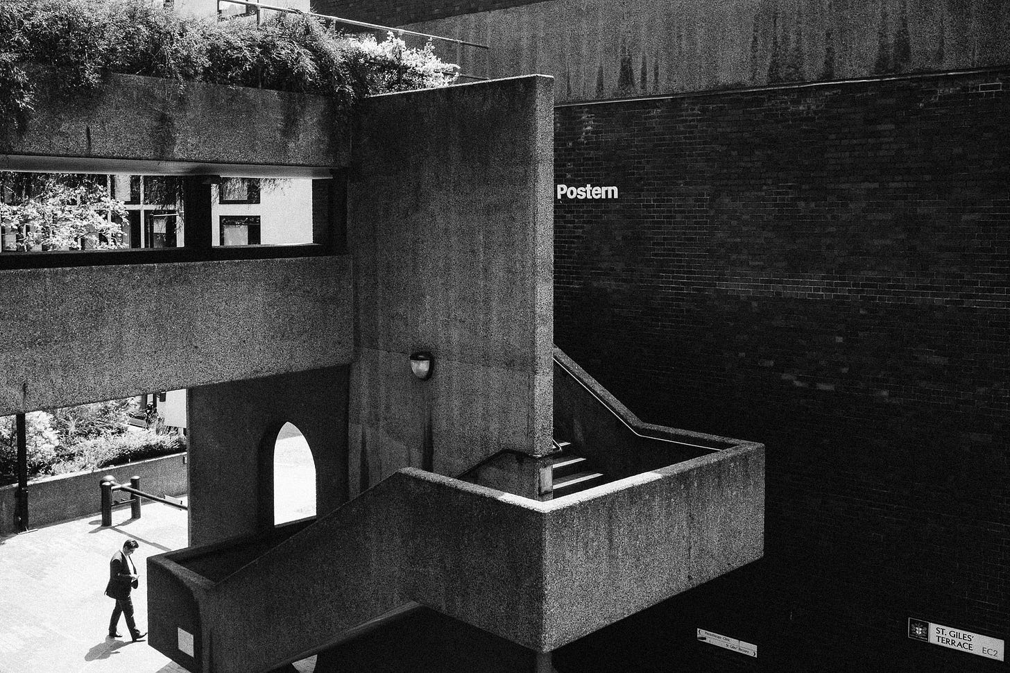 The Barbican in London. A man stands at the bottom of a brutalist outdoor concrete staircase.