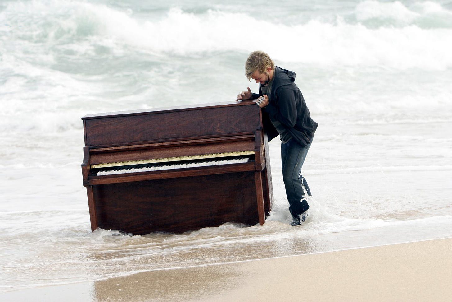 Charlie (Dominick Monaghan) struggles to open the top of a piano that is standing in the ocean.