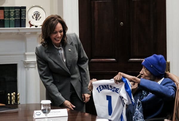 Vice President Kamala Harris accepts a white-and-blue basketball jersey, with the No. 1 and “Tennessee” printed on it, from Dick Barnett.