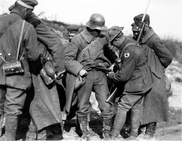 Black and white photo of German prisoners having their pockets turned out by an Australian soldier.