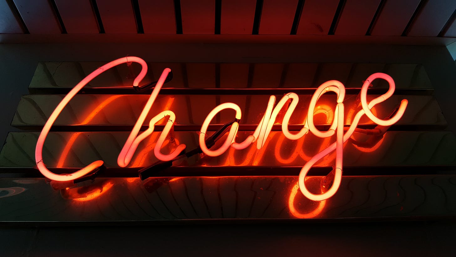 An orange neon "Change" sign in cursive writing against a dark background.
