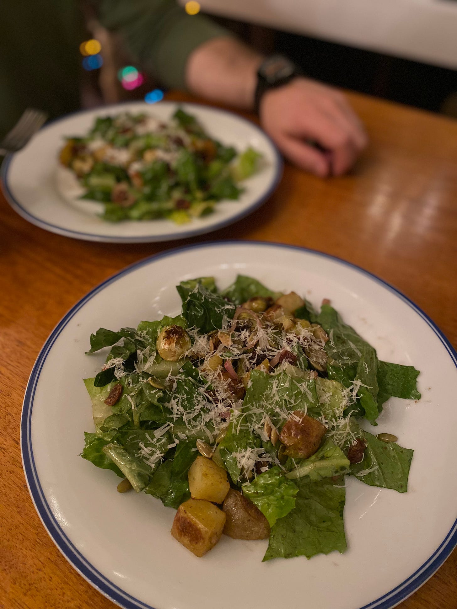 Two white dinner plates with blue rims, each with a serving of the roasted vegetable & romaine salad described above, topped with parmesan, pepitas, and raisins.