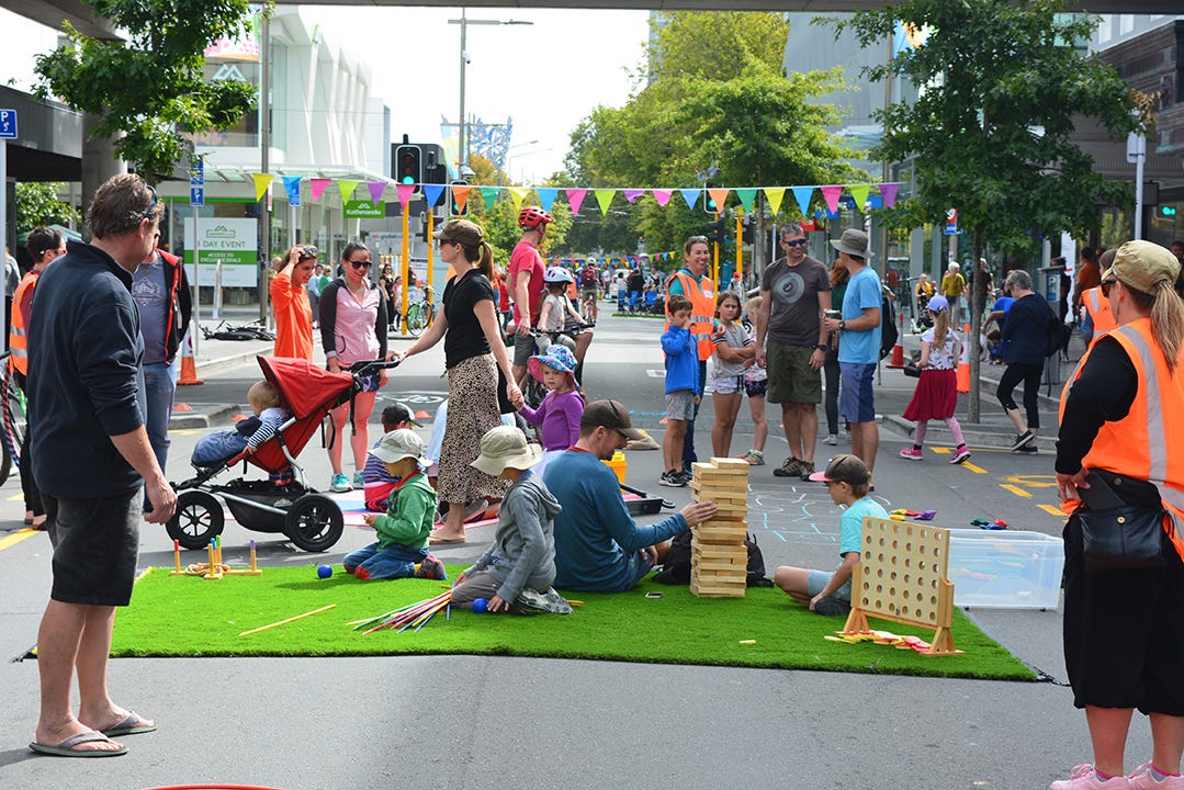 People sitting on artificial turf in the middle of the street playing games.