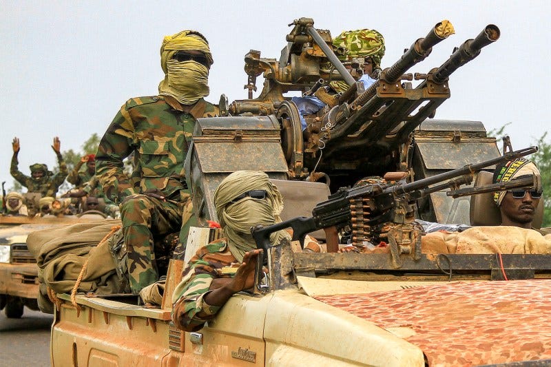 Sudanese fighters wearing face coverings ride in a vehicle in a military convoy accompanying the governor of Sudan's Darfur region.