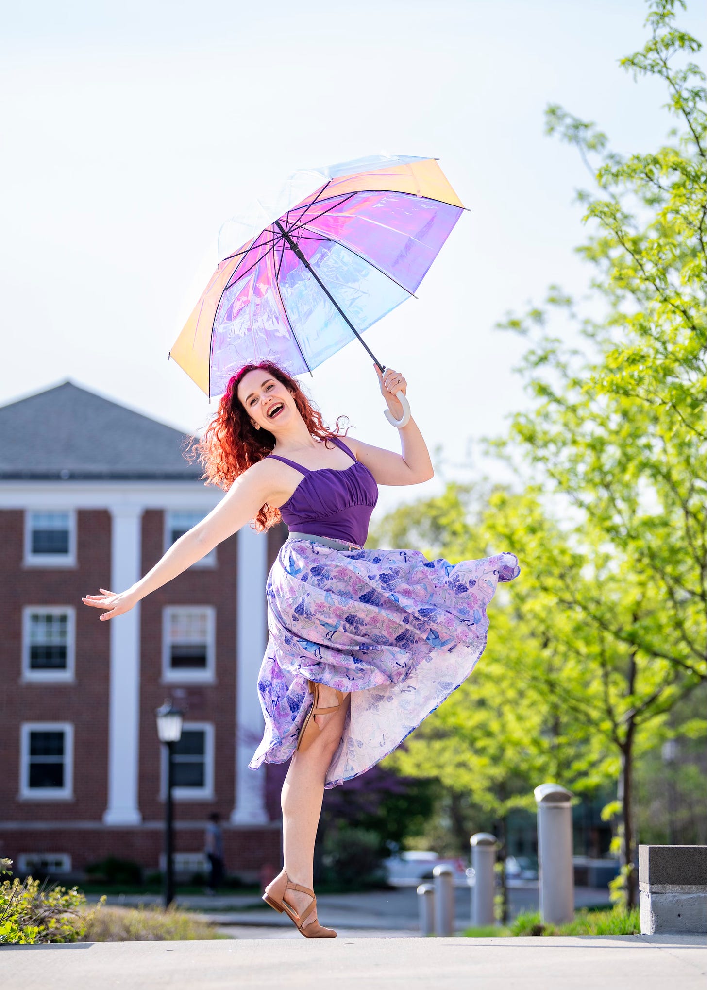 A woman in a purple top and skirt dances while lifting an umbrella