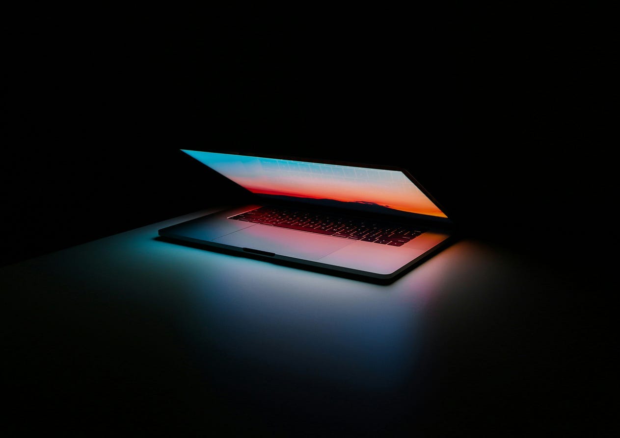 Photo of an Apple laptop glowing futuristically inside of a dark room / taken by Ales Nesetril on Unsplash