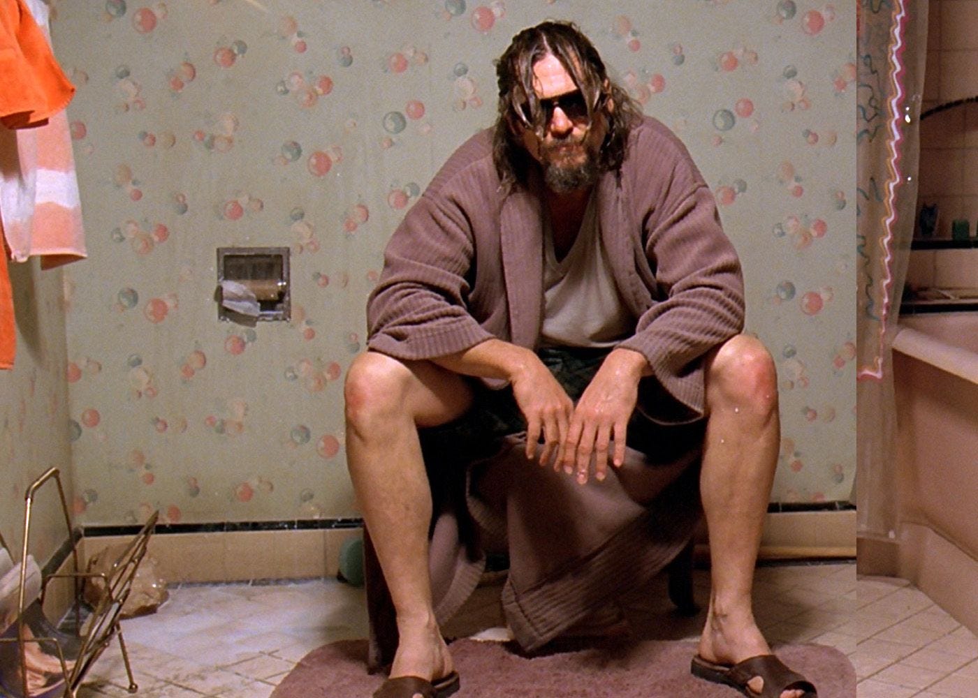 The Dude sits on a toilet contemplating his misfortune.