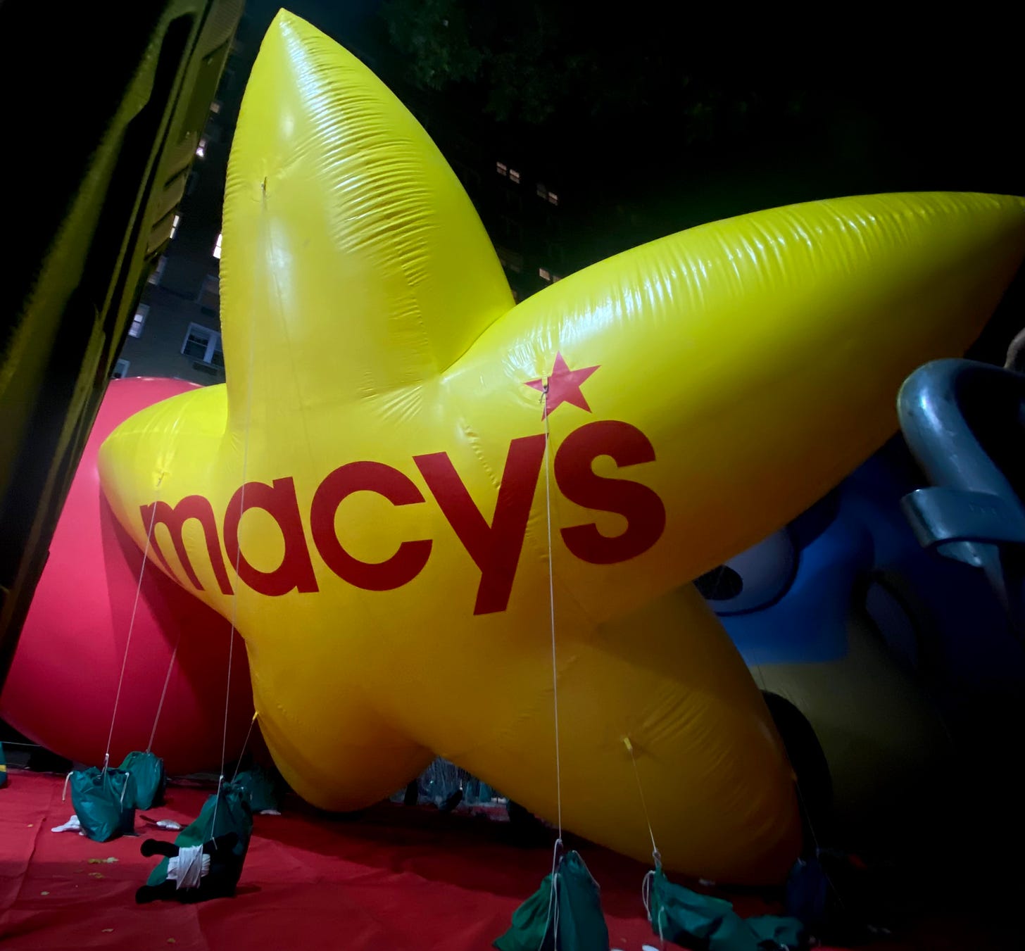 A large yellow balloon in the shape of a star with Macy's written in red letters. It is in the street on the Upper West Side, held down by sandbags.