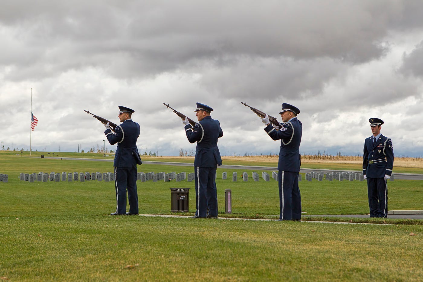 A military three-rifle salute for a funeral with the American flag on a hill in the background at half mast