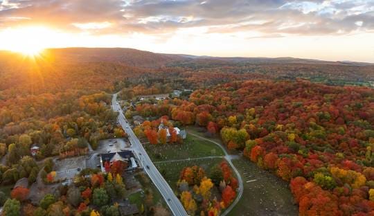 Aerial view of Chelsea, Quebec, multicoloured trees in the fall, with the sun setting over the mountains