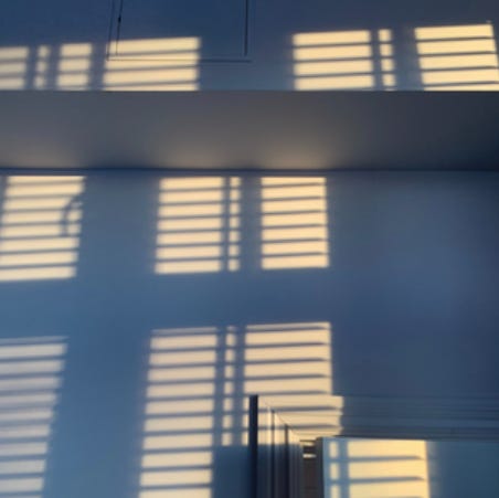 A photo of light and shadows on a wall, cast by venetian blinds