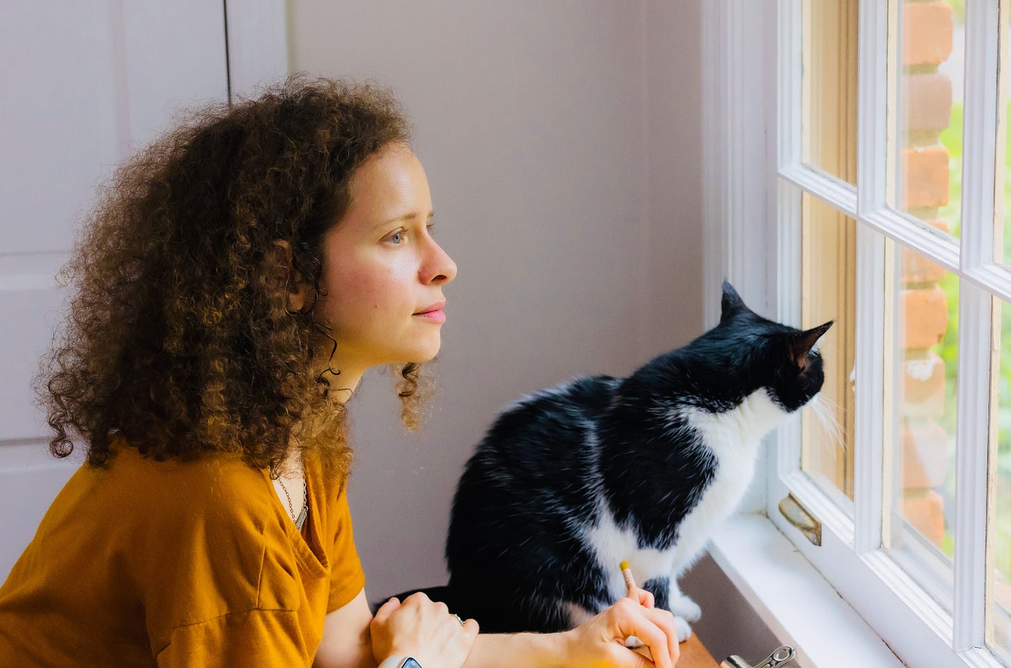 A woman with dark hair and a black and white cat staring out the window