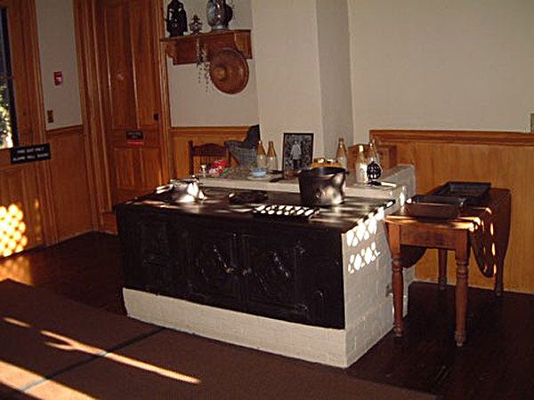 a old style coal stove in the kitchen with pots and pants on top -- See Caption Below