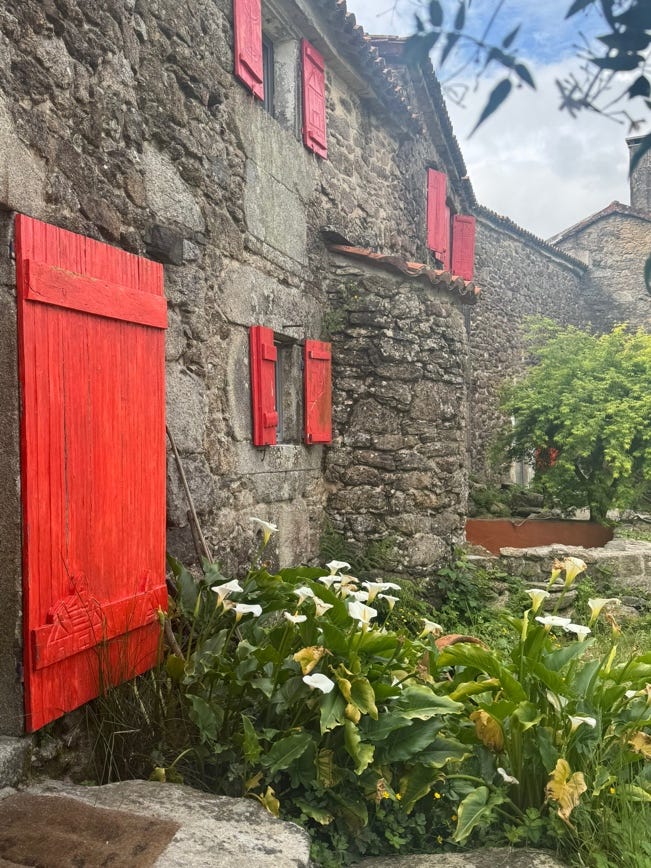 A stone building with red shutters

Description automatically generated