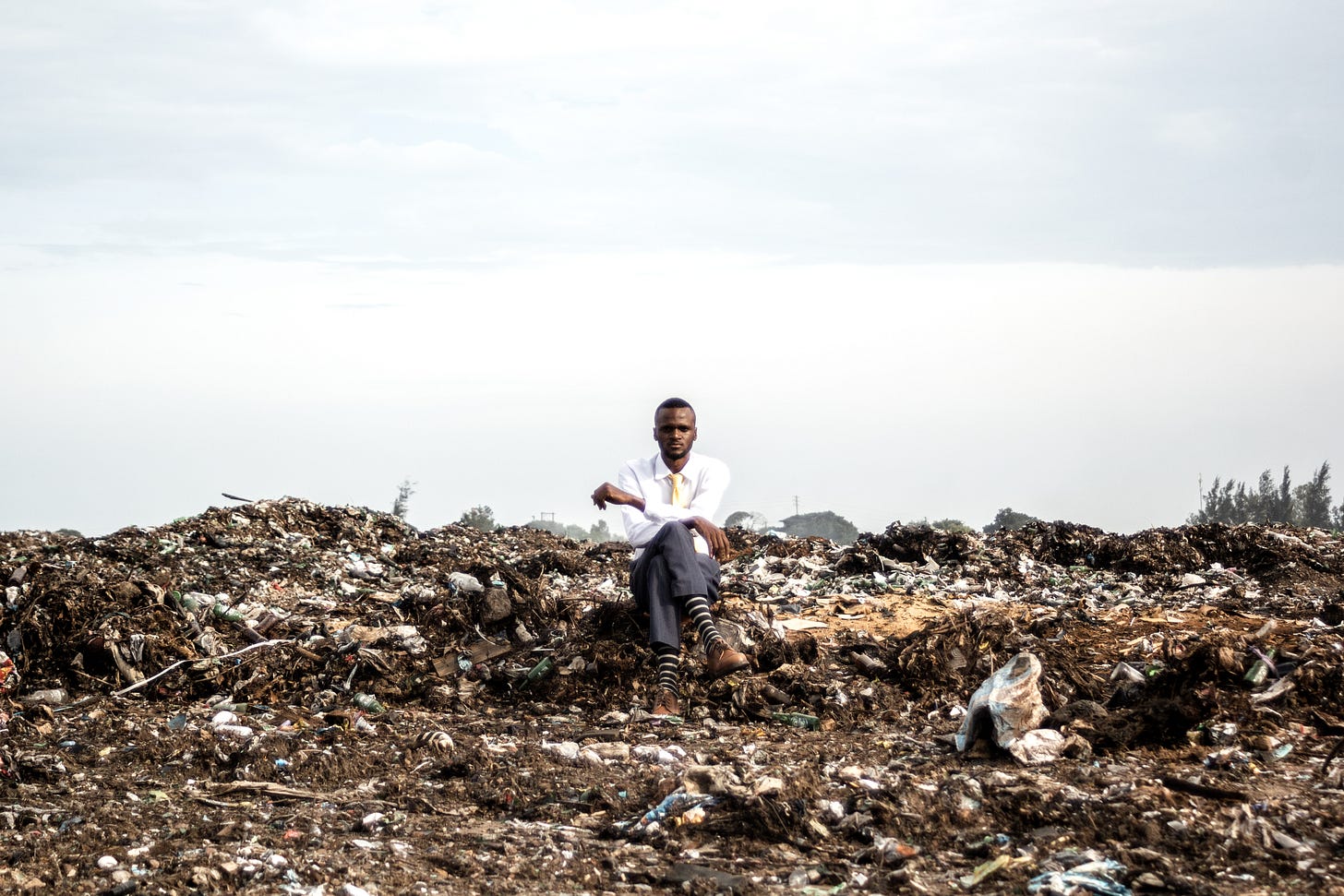 A man dressed in a suit sitting on top of a trash dump
