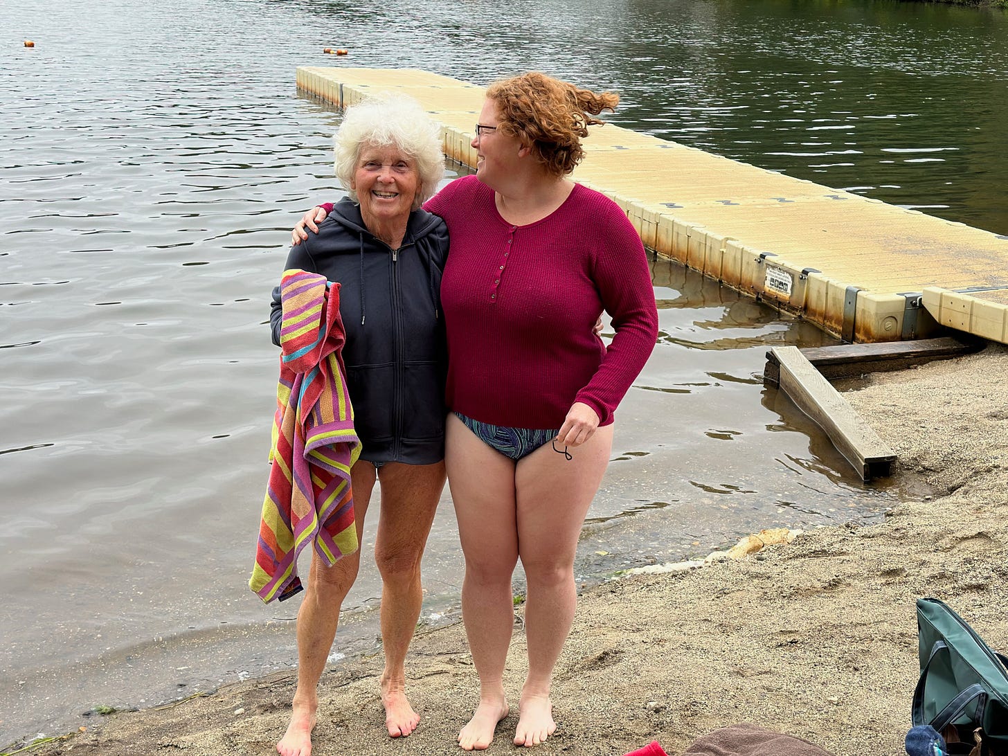 My mom and I standing at the edge of the lake with our arms around each other, the dock behind us.My mom is smiling at the camera, and I’m smiling at her.