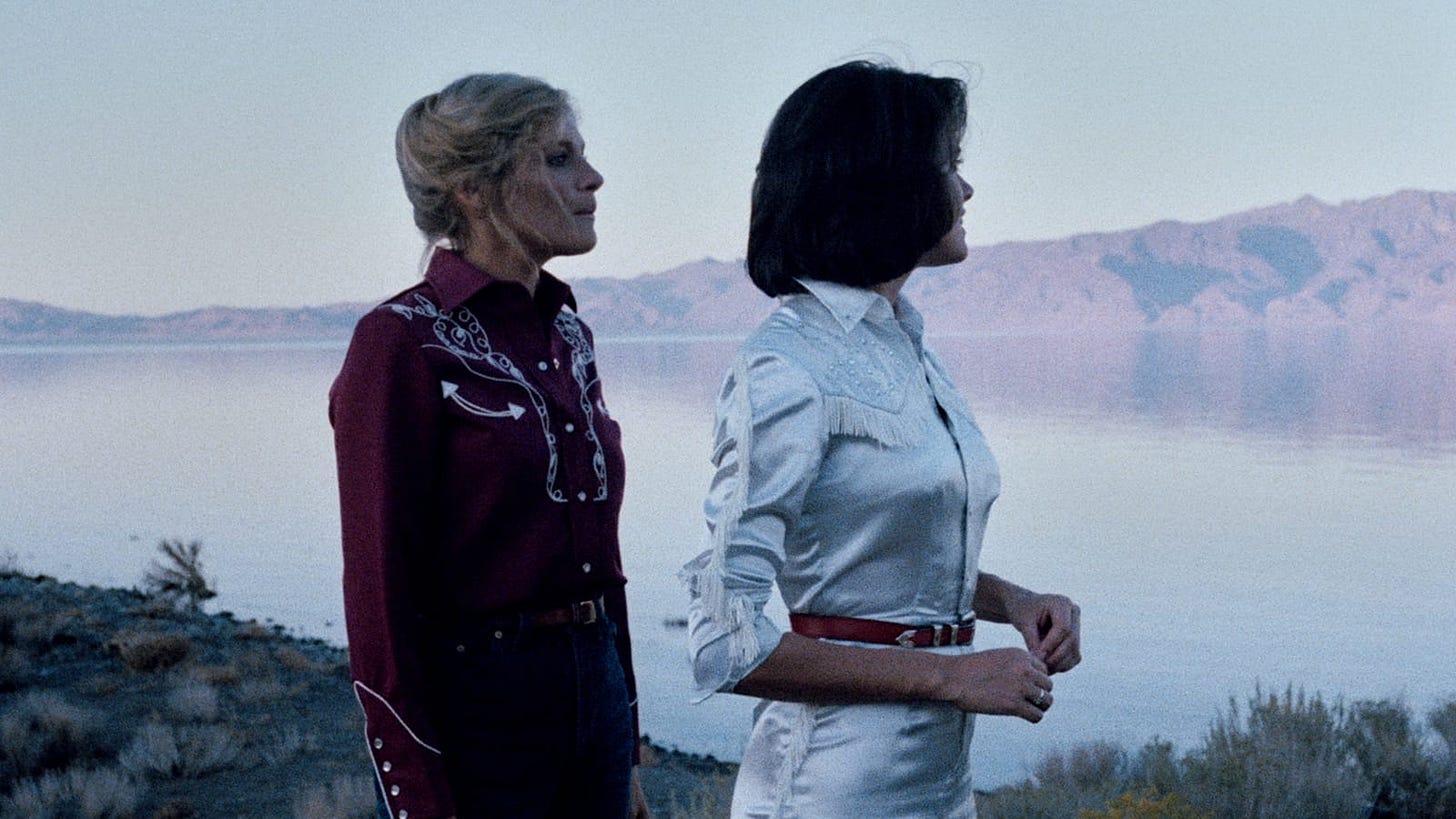 Movie still from Desert Hearts. Two women in cowboy outfits walk by a peaceful lake and mountain