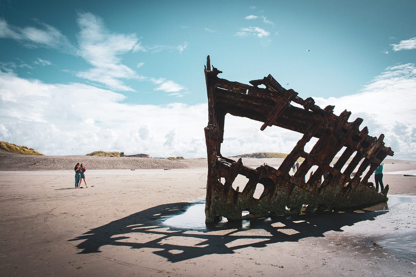old shipwreck washed up on a beach with people looking at it