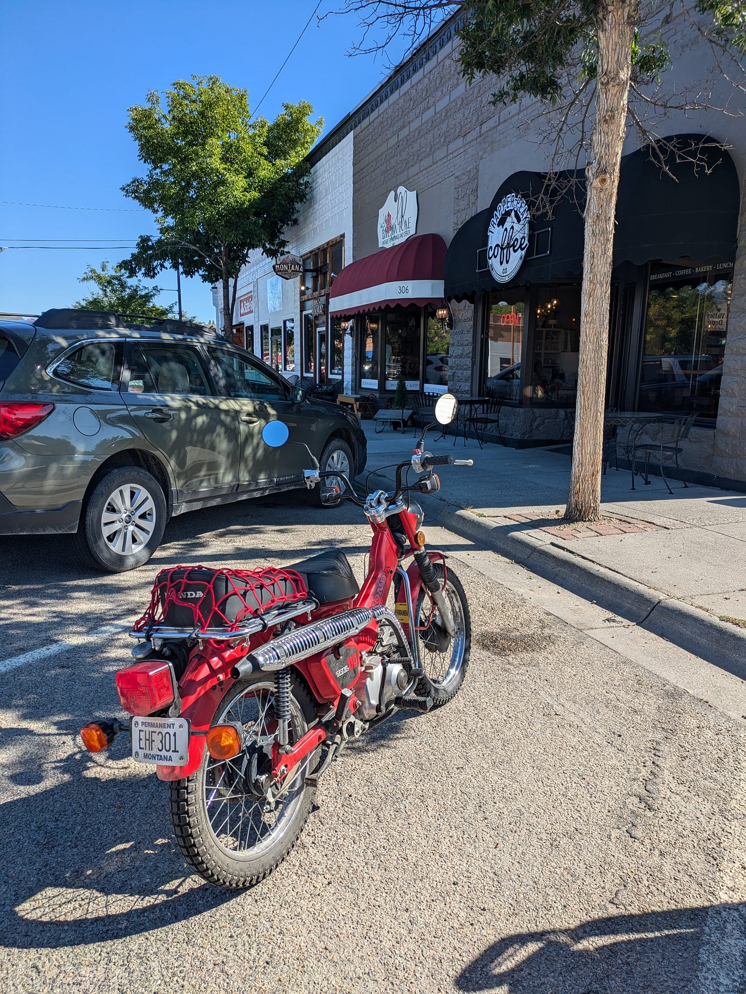 a vintage red motorbike parked outside a coffee shop on the street of a small town