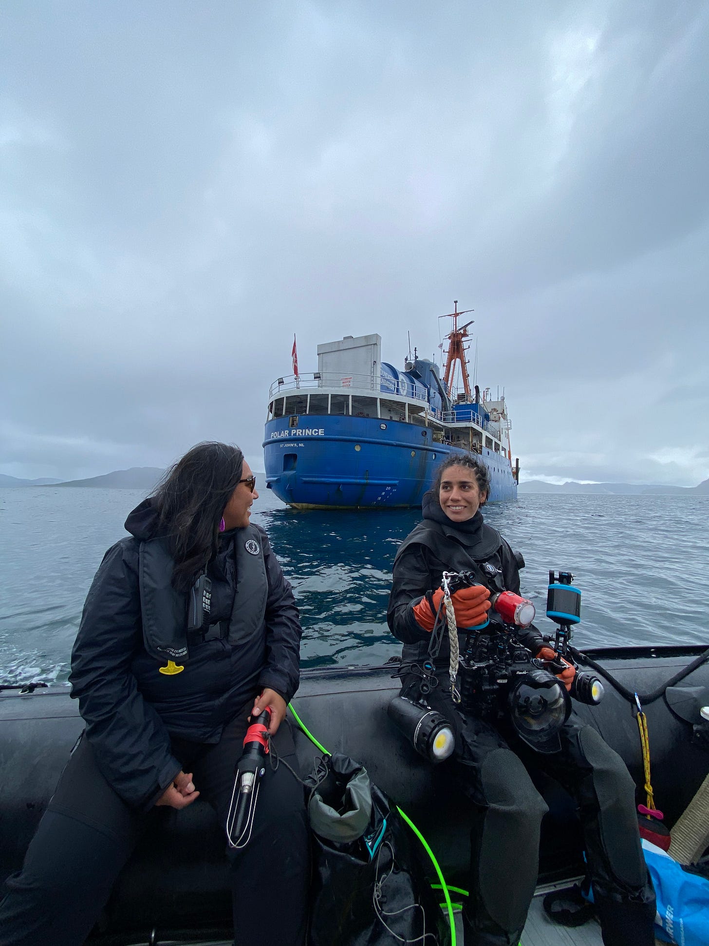 Anna and Rosie sitting on the edge of the zodiac with the Polar Prince ship in the background.