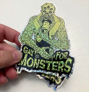 a sparkly "gay for monsters" sticker with an illustration of a monster and man embracing