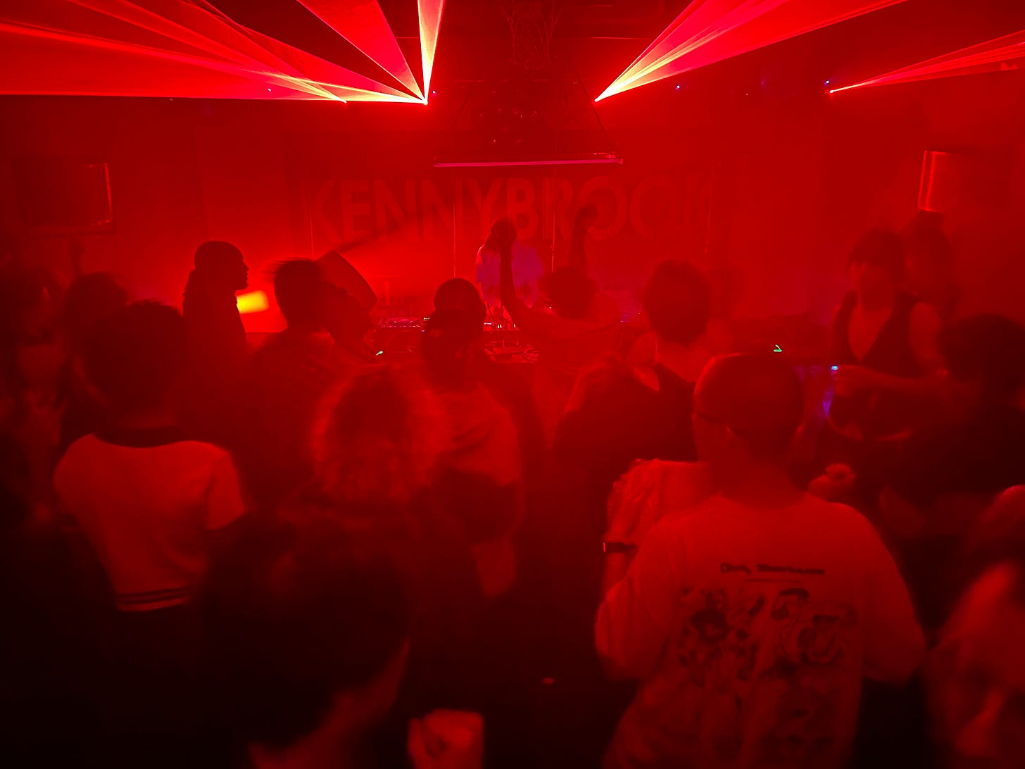 DJ performing in front of ravers under red lights and lasers