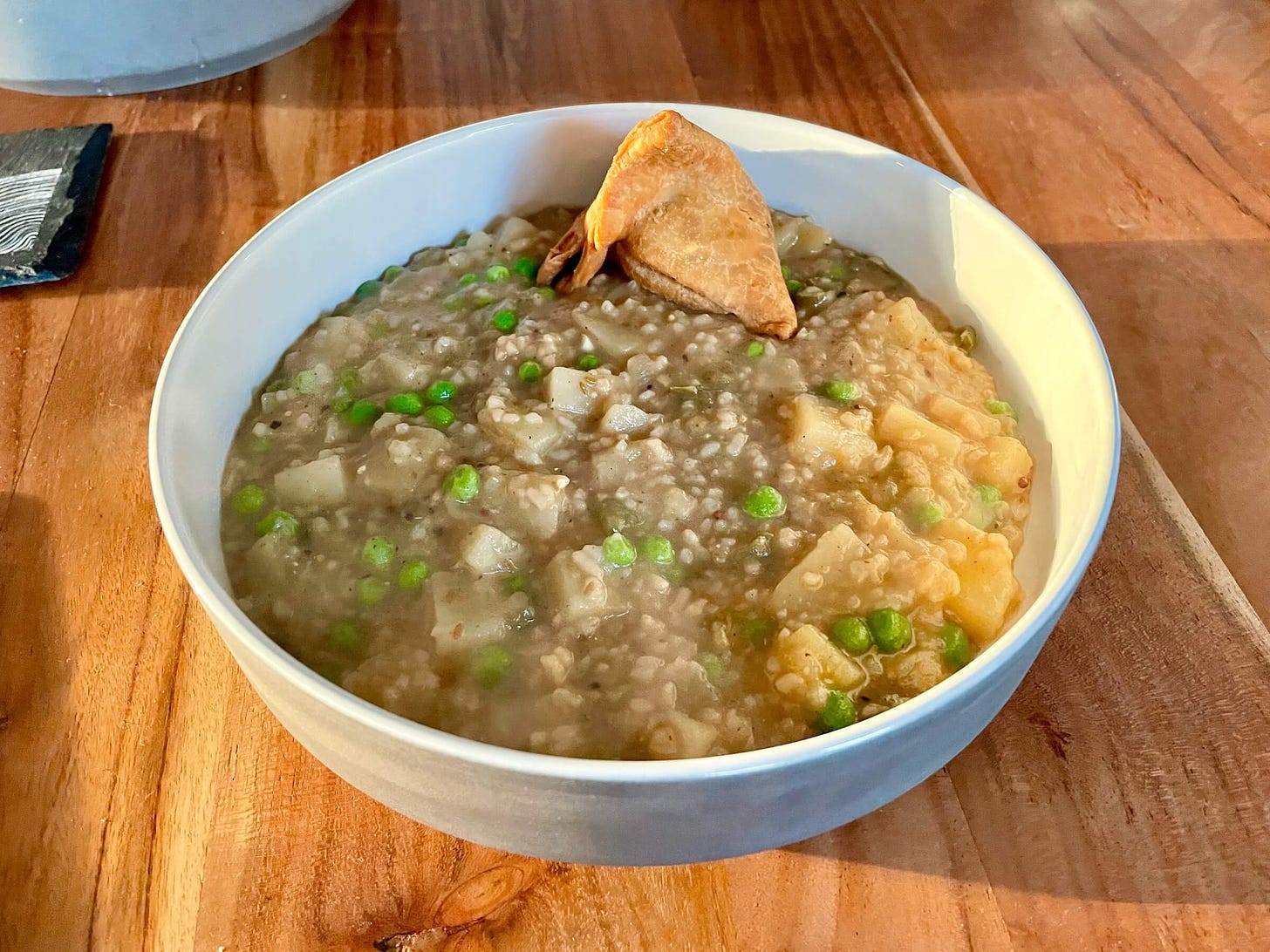 A grey bowl of risotto with potatoes and peas, and a samosa perched at the far side.