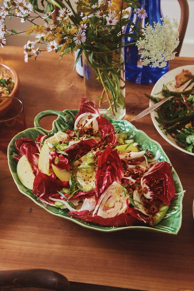 A leaf-shaped serving platter filled with a seasonal salad of bitter lettuce and pecans