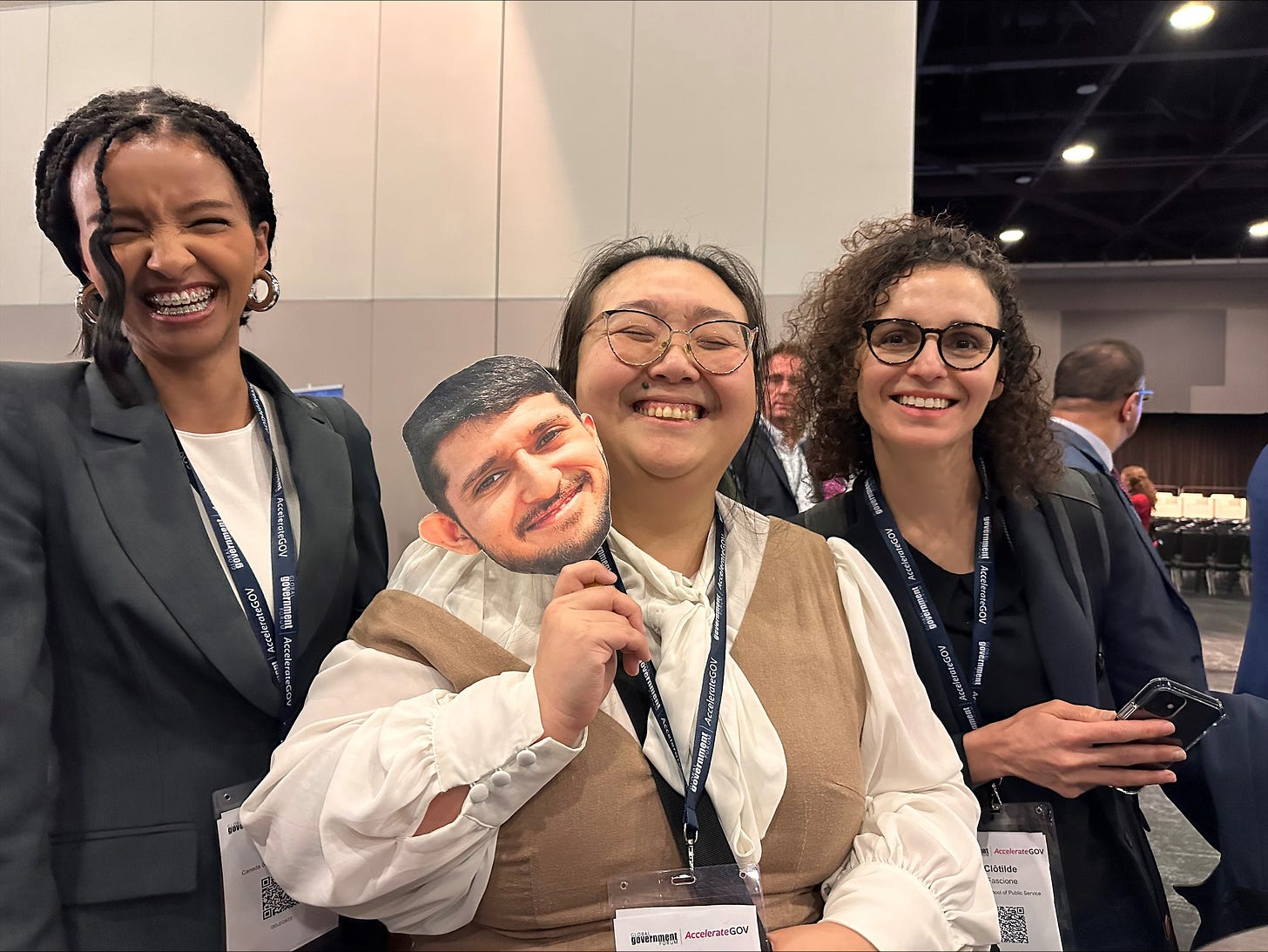 Lello, Heidi, and Clotilde laughing together at AccelerateGov. Heidi holds a cardboard cutout of Lajendon.