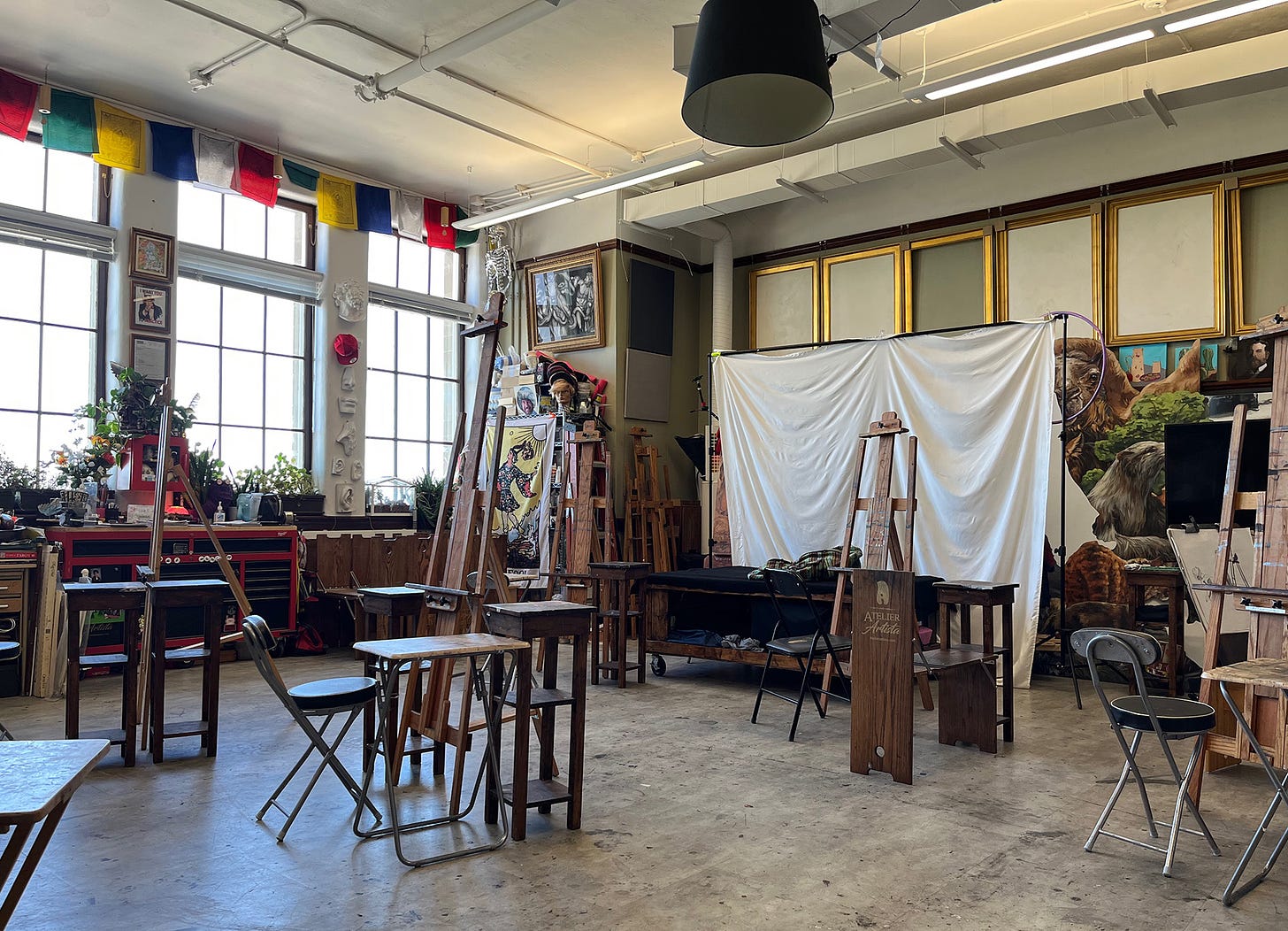 Empty painting studio with several statios of easels, chairs and little tables.