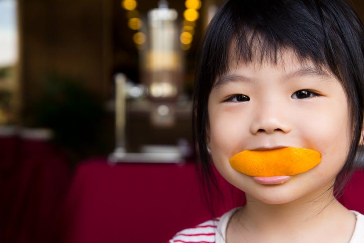 A child has an orange rind for a smile.