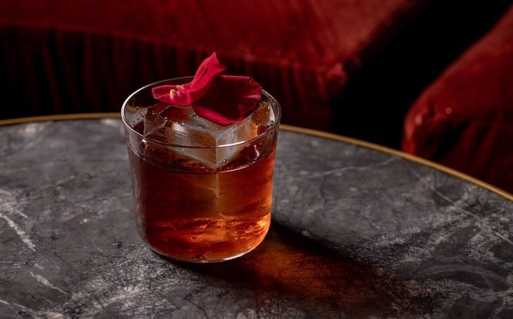 A cocktail with red petals perched on the ice cube