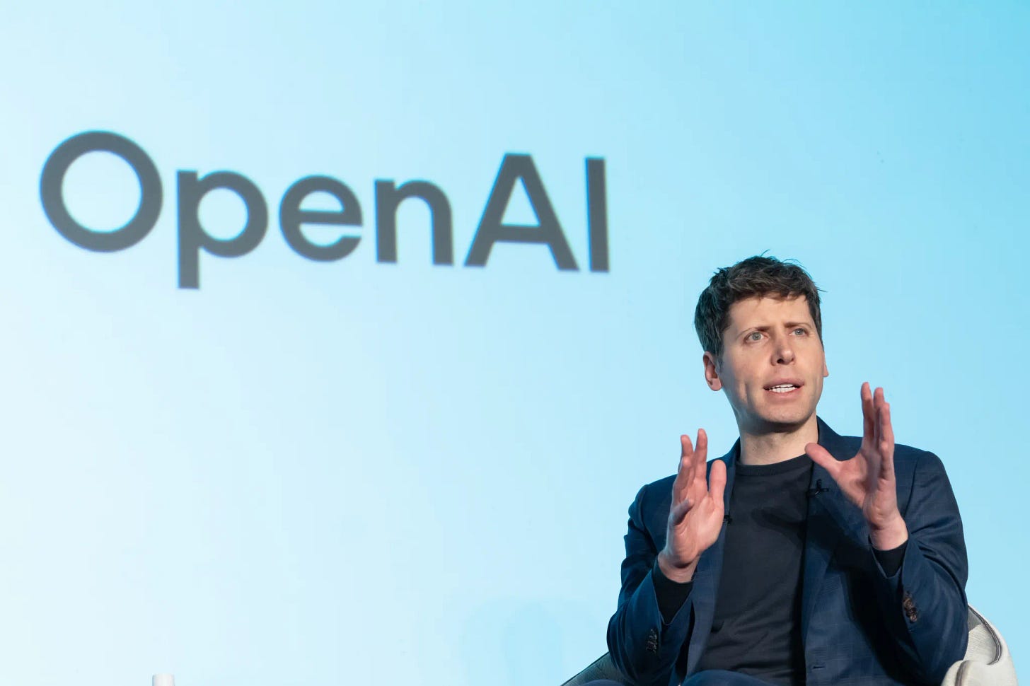 Sam Altman speaking in front of a wall that says OpenAI